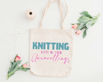 Może przedstawiać: Biała torba z płótna z napisem "Knitting keeps me from unraveling" w niebieskich i różowych literach. Torba ma długi uchwyt i stoi na białym tle.