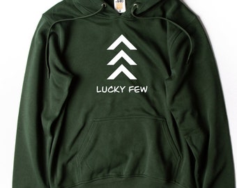 Puede incluir: Una sudadera con capucha de color verde oscuro con un gráfico blanco de tres flechas apuntando hacia arriba y el texto "LUCKY FEW" debajo de las flechas.