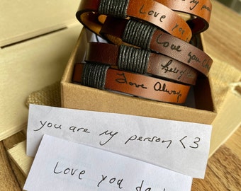 May include: A set of four brown leather bracelets with black string accents. Each bracelet has a handwritten message engraved on it. The messages are "you are my person", "Love you", "Love you always", and "Love you Ch". The bracelets are packaged in a brown box with a handwritten note that says "you are my person <3 Love you dad".