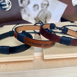 May include: Two leather bracelets with adjustable closures. One bracelet is black and the other is brown with the text "forever in our" engraved on it.