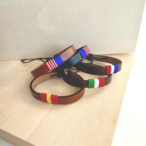 May include: Four leather bracelets with different colored woven flag designs. The bracelets are brown, black, and brown.