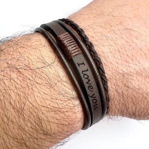 May include: A brown leather bracelet with a braided leather strap and the words "I love you" engraved on the main strap.