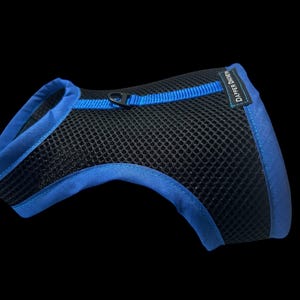 May include: Black mesh pet harness with blue trim and accents. The harness has a breathable design and a buckle closure. The brand name "Dapper Dawg" is visible on the side. This pet accessory is designed for comfort and safety.
