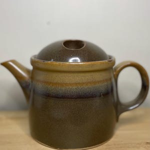 May include: A brown ceramic teapot with a lid and a brown and tan glaze. The teapot has a spout and a handle.