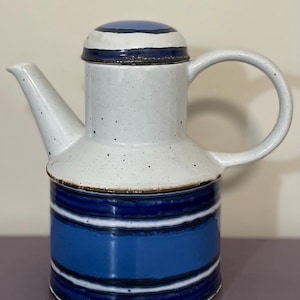 May include: A ceramic coffee pot with a white speckled upper section and a blue and white striped lower section. The lid and handle are white, and the spout is angled. The pot is designed for serving beverages.