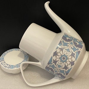 May include: White ceramic teapot with a blue and grey floral pattern. The teapot has a lid and a handle. There is a matching lid for the teapot.