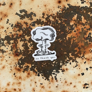 May include: A white sticker with a black and white illustration of a mushroom cloud with the text "POOF YOU'RE JUST CLOUD" above it and "no thank you." below it. The sticker is on a rusty metal surface.