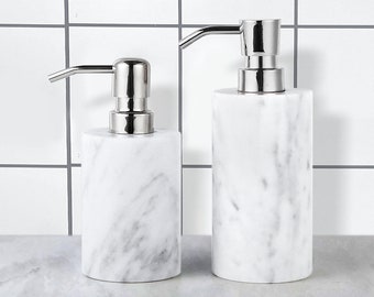 May include: Two white marble soap dispensers with silver pumps. The dispensers are cylindrical and have a textured marble finish.