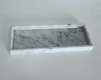 May include: A white marble rectangular tray with a smooth surface. The tray has a raised edge around the perimeter.