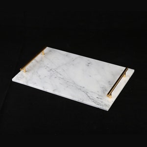May include: White marble serving tray with gold metal handles. The tray is rectangular and has a smooth surface.