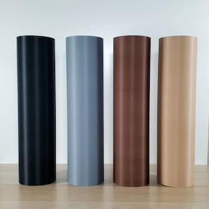 May include: Four cylindrical objects in a row, each a different solid color: black, gray, brown, and tan. The cylinders are standing upright on a light-colored wooden surface against a white background.