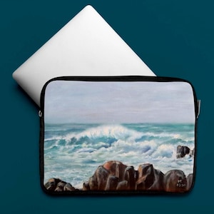 May include: A black laptop sleeve featuring an ocean wave painting. The artwork depicts a seascape with crashing waves, rocks, and a cloudy sky. A white laptop is partially visible above the sleeve.