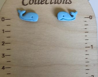 May include: A pair of light blue whale-shaped stud earrings displayed on a light wood card with the text Val Cal Collections. The card features a printed ruler on both sides, with the left side showing inches and the right side showing centimeters.