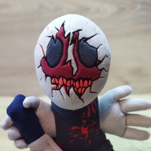 May include: A plush toy of a character with a white head, red and black eyes, and a red mouth with sharp teeth. The character is wearing a dark blue shirt with red splatters and is holding a grey knife.