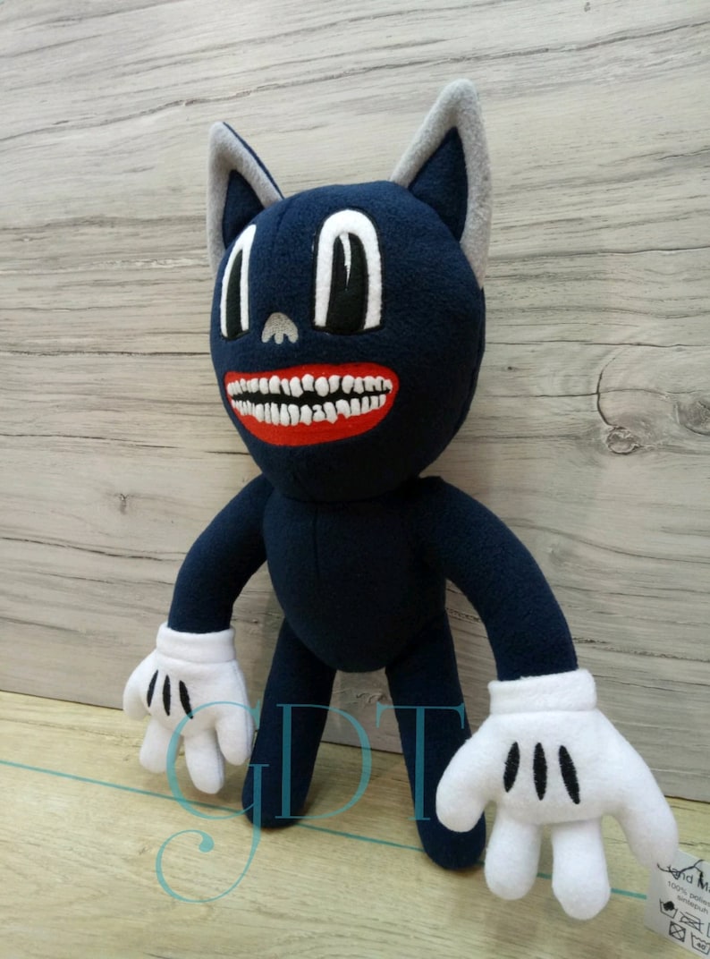 May include: A blue cartoon cat plush toy with a large toothy grin and white gloves. The toy has large black eyes and a gray nose. The toy is standing on a wooden surface.
