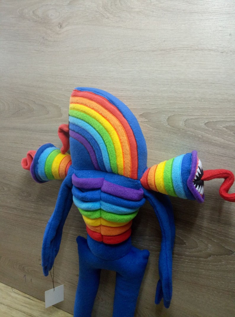 Puede incluir: Un juguete de peluche de color arco&iacute;ris con un cuerpo largo y delgado y una cabeza grande. El juguete tiene una cabeza de color arco&iacute;ris y un torso de color arco&iacute;ris. El juguete tiene una cola larga y delgada y dos brazos largos y delgados. El juguete est&aacute; hecho de tela suave y de felpa.