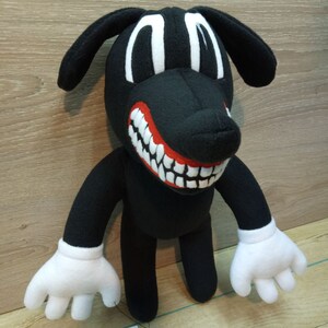 May include: Black plush cartoon dog with a large red mouth and white teeth. The dog has white eyes and white gloves. The dog is standing on a wooden surface. A tag attached to the dog reads 'Hand-Made 100% polyester  cotton' with icons for washing instructions.