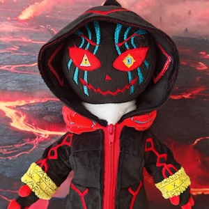 May include: A plush doll featuring a black hooded jacket with a red zipper, red accents, and yellow cuffs printed with the text WARNING. The doll has a black face with embroidered red eyes, blue facial markings, and a stitched red mouth.