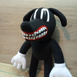 May include: A black plush cartoon dog with white eyes, a red mouth with white teeth, and white gloves. The dog is standing on a wood surface. The tag attached to the dog reads 'Handmade with love, wash delicate, do not bleach, do not tumble dry, iron low, do not dry clean.'
