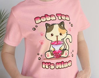 May include: Pink t-shirt with a cartoon cat drinking boba tea. The text on the shirt says "Boba Tea It's Mine".
