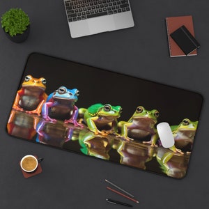 May include: A colorful mousepad featuring five frogs in various poses. The frogs are green, blue, orange, yellow, and red. The mousepad is black with a reflective surface.