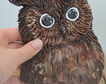 May include: A brown owl sculpture with painted eyes. The owl is made of wood and has a textured surface.