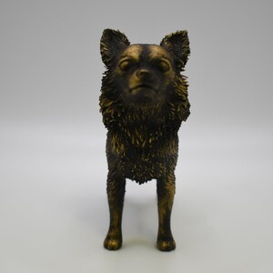 Pu&ograve; includere: Una statuetta dorata di un chihuahua in piedi su tutte e quattro le zampe. Il cane ha un pelo corto e liscio e guarda direttamente la telecamera.