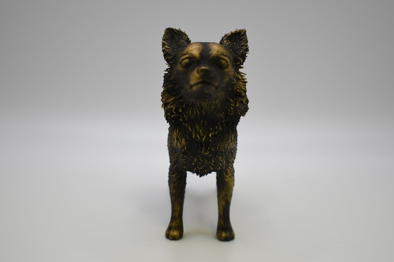 Pu&ograve; includere: Una statuetta dorata di un chihuahua in piedi su tutte e quattro le zampe. Il cane ha un pelo corto e liscio e guarda direttamente la telecamera.