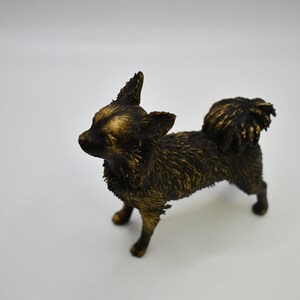 Pu&ograve; includere: Una piccola statuetta di chihuahua nera e dorata. La statuetta &egrave; in piedi su tutte e quattro le zampe e ha la testa inclinata di lato. La statuetta &egrave; realizzata in un materiale liscio e lucido.
