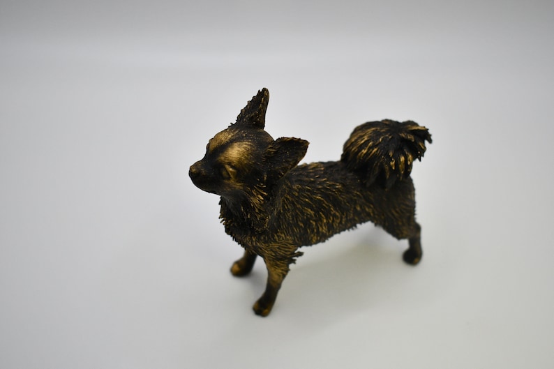 Pu&ograve; includere: Una piccola statuetta di chihuahua nera e dorata. La statuetta &egrave; in piedi su tutte e quattro le zampe e ha la testa inclinata di lato. La statuetta &egrave; realizzata in un materiale liscio e lucido.