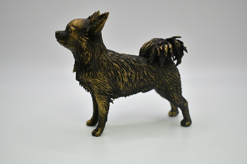Pu&ograve; includere: Una piccola statuetta dorata di un chihuahua. La statuetta &egrave; in piedi su tutte e quattro le zampe con la coda arrotolata. La statuetta &egrave; realizzata in un materiale liscio e lucido.