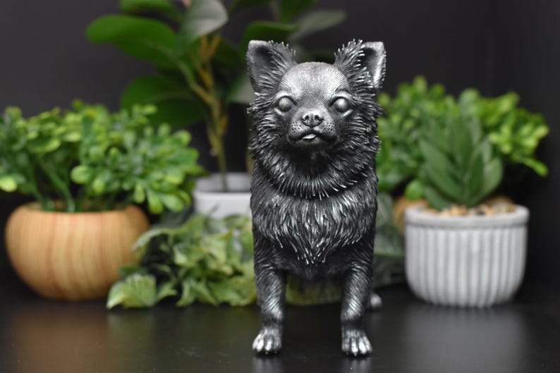 Puede incluir: Una figurita de chihuahua de color plateado de pie sobre una superficie negra. La figurita est&aacute; detallada con pelo y tiene un aspecto realista.