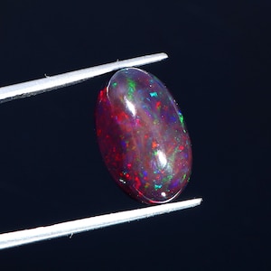 Op de afbeelding: Een ovale, donkerrode opaal edelsteen met flitsen van groen en blauw.