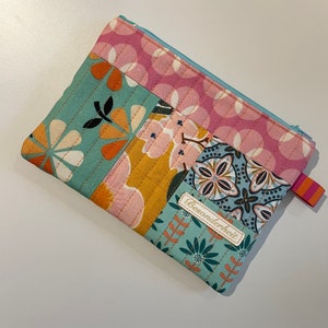 Könnte beinhalten: Eine Patchwork-Stofftasche mit Reißverschluss und floralem und geometrischem Muster. Die Tasche hat ein weißes Etikett mit dem Wort "Besonderheit" darauf.