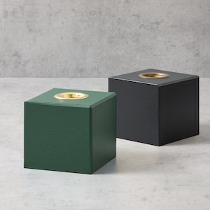 May include: Two square-shaped display stands with a small circular indentation on top. One stand is green and the other is black.