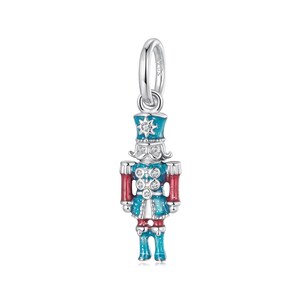 May include: A silver charm depicting a toy soldier nutcracker. The charm is painted in blue, red, and white, with clear crystal accents. The nutcracker has a tall hat and a mustache. The charm is suspended from a silver loop.