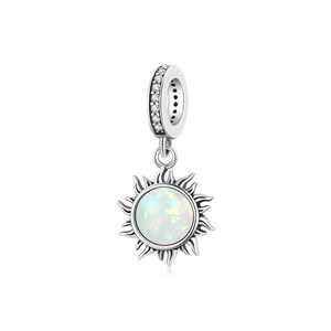 May include: A silver charm featuring a sun design. The sun has a white opal center and detailed rays. The top loop is adorned with small, clear crystals. This charm is designed to be added to a bracelet or necklace.