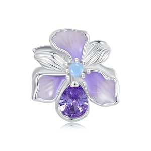 Pode incluir: Um amuleto de prata em forma de flor com esmalte roxo e azul e cristais.