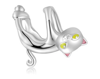 May include: Silver cat charm with green eyes and pink ears. The cat is hanging upside down with its paws curled up.