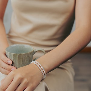 May include: A woman wearing a beige satin dress with a double strand pearl bracelet on her wrist.