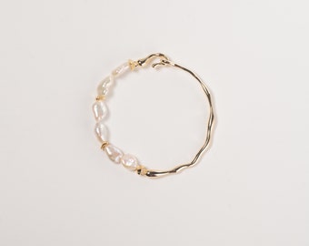 Peut inclure: Un bracelet jonc en or avec une forme irrégulière texturée. Le bracelet est orné d'une rangée de perles blanches.