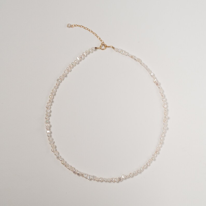 May include: A delicate pearl necklace with a gold clasp. The necklace is made of small, irregular pearls that are strung together on a thin gold chain.