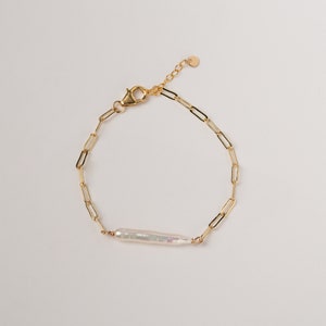 Puede incluir: Un brazalete de cadena dorada con un colgante de perla blanca.