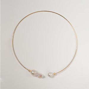 May include: A gold choker necklace with two white baroque pearls attached.