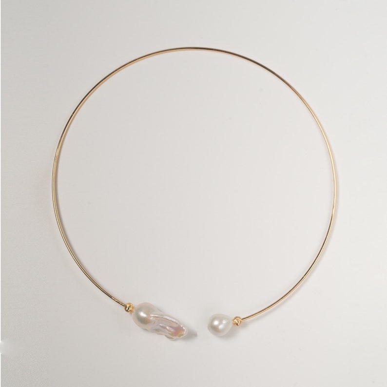 May include: A gold choker necklace with two white baroque pearls attached.