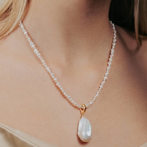 May include: A delicate pearl necklace with a large, irregular pearl pendant. The necklace is made of small, white pearls and has a gold clasp.