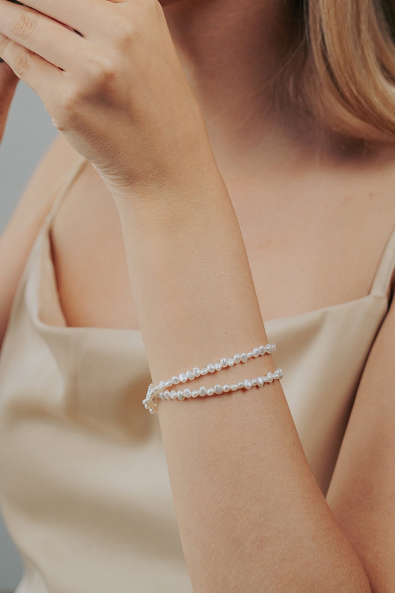 May include: A double-strand pearl bracelet with small, irregular pearls. The bracelet is made of white pearls and is worn on a person's wrist.