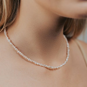 May include: A delicate pearl necklace with small, irregular pearls. The necklace is made of white pearls and is worn by a person with fair skin.