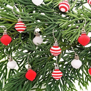 May include: A pair of Christmas ornament earrings with red and white striped ornaments and solid red and white ornaments.