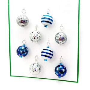 May include: Eight silver and blue Christmas ornaments with white and blue patterns. The ornaments are hanging from silver hooks.